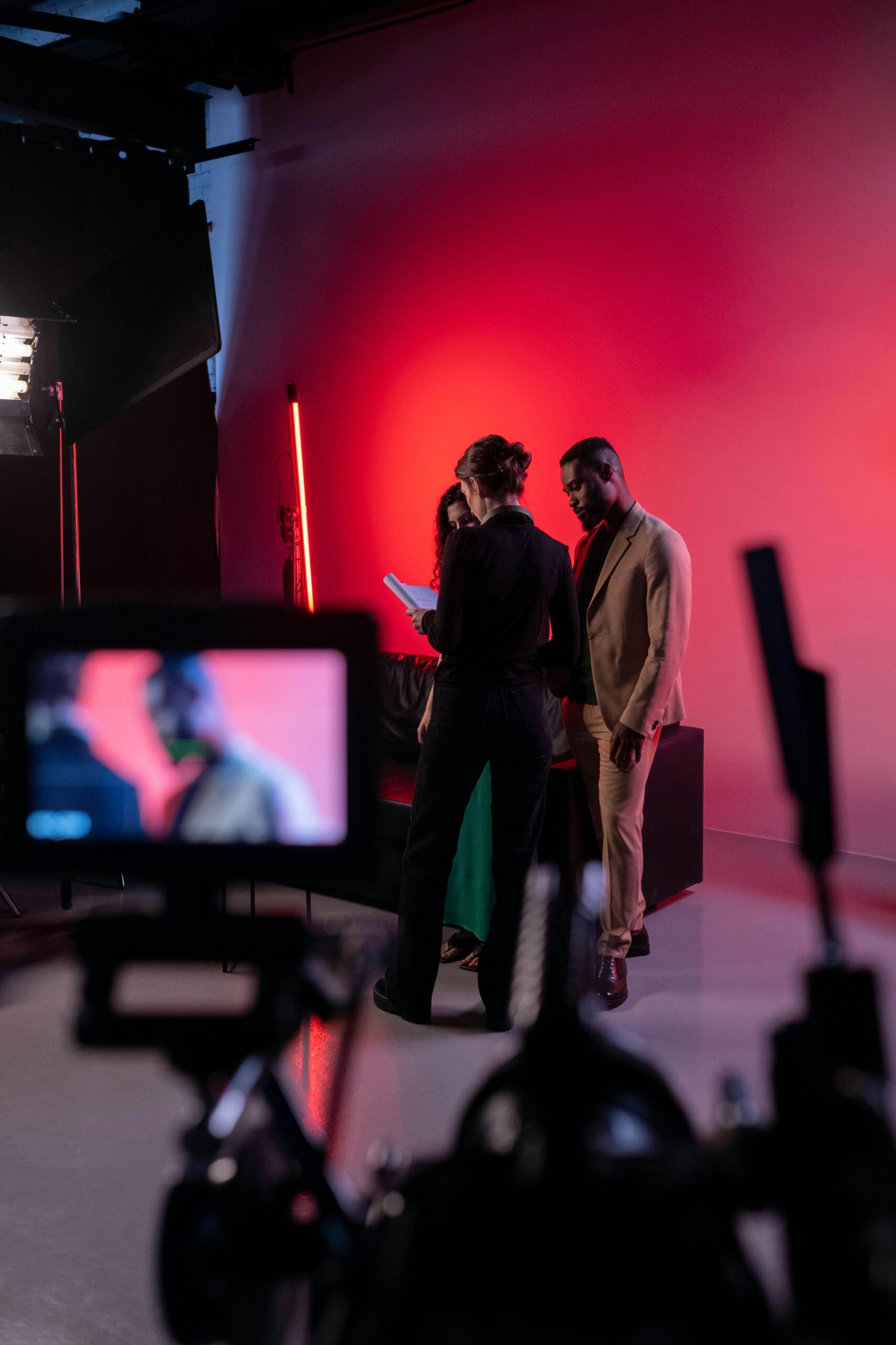 Film set with actors and crew in a studio with vibrant red lighting.